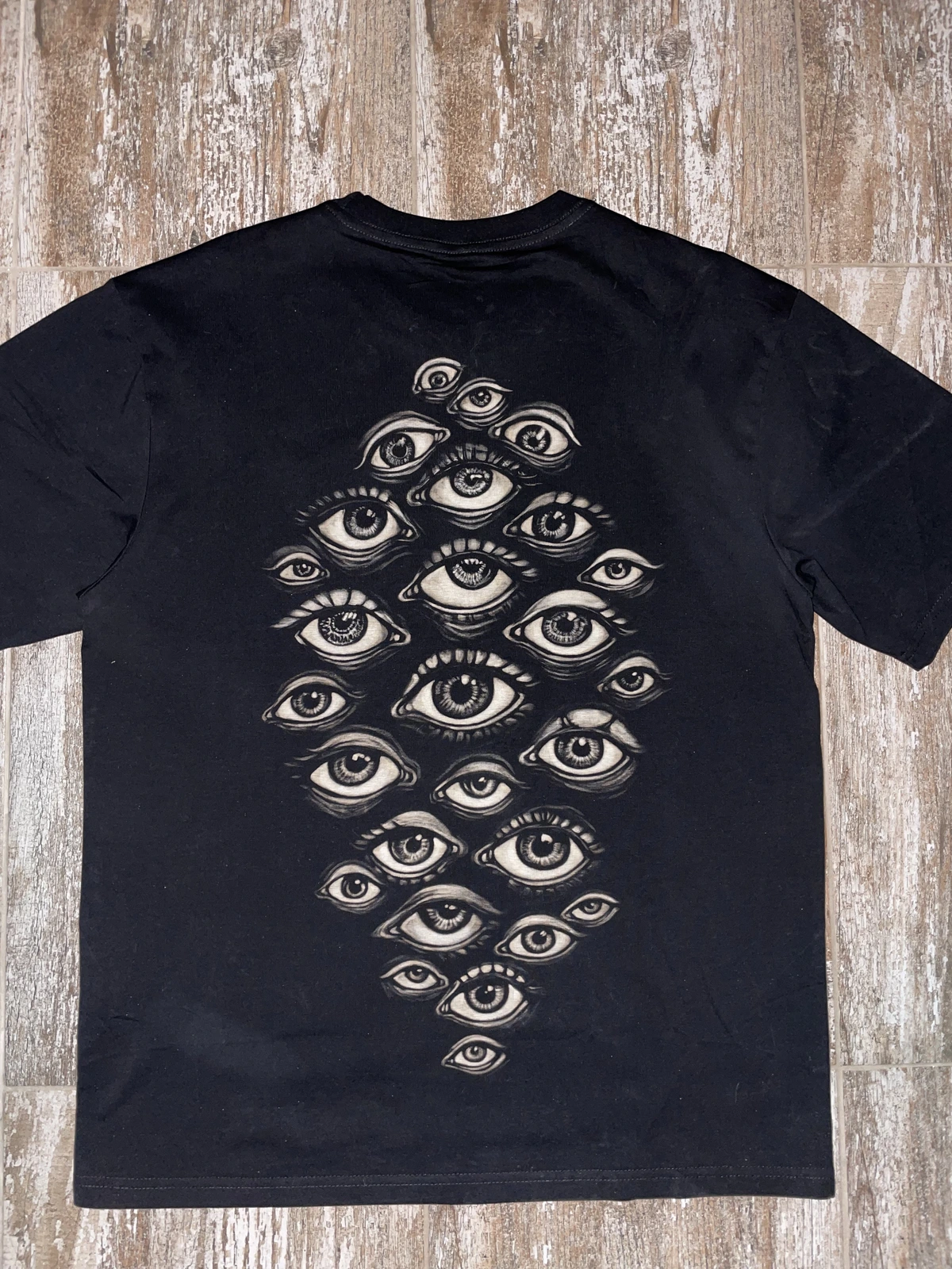 Minimal evil eye bleach shirt design featuring multiple protective eye symbols on black cotton
