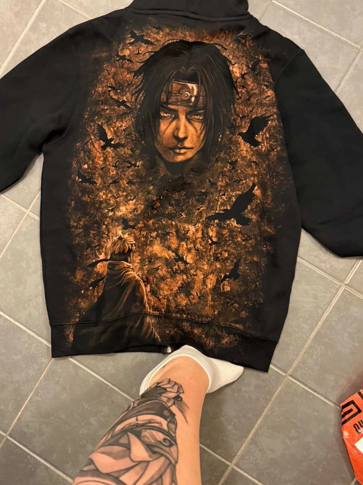 Ein Kunde steht neben einem schwarzen, von Itachi inspirierten Hoodie, auf dessen Rückseite handgefertigte Kunstwerke zu sehen sind.