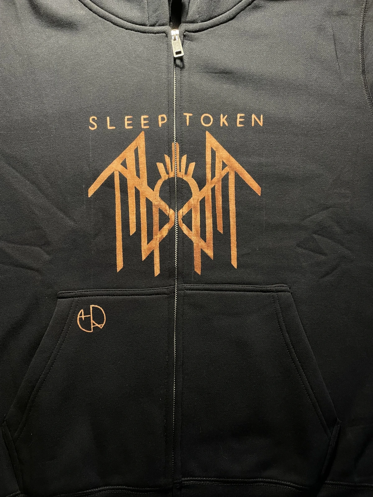 Vorderseite eines schwarzen Kapuzenpullovers mit Reißverschluss, der mit einem vom Sleep Token inspirierten Symbol und Schriftzug versehen ist, der durch den Reißverschluss geteilt wird.