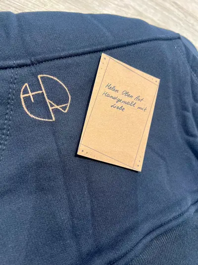 Close-up of a hand-painted hoodie with the Helen Oben Art logo and a care instruction card included with the order