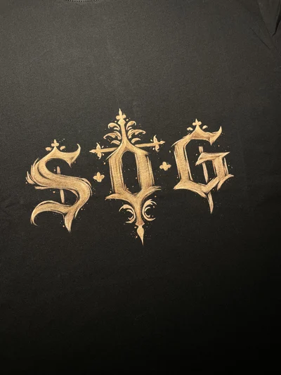 Close-up of S.O.G initials painted in gothic lettering on the front of the t-shirt