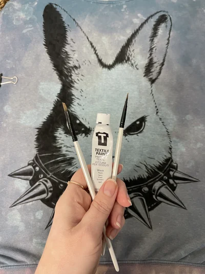 Finished hand-painted blue sweatshirt with angry bunny design and textile paints used in the process