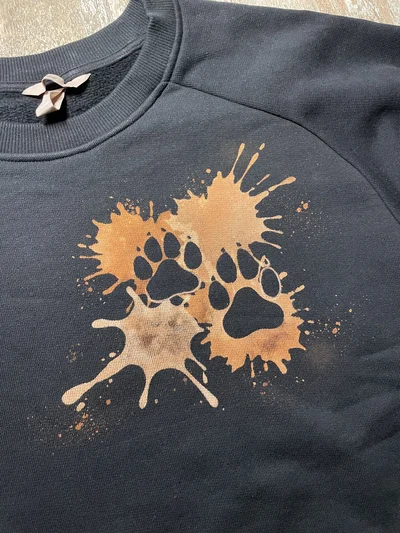 Nahaufnahme des minimalistischen Vorderseitenmotivs mit zwei Hundepfotenabdrücken auf handgemalten Bleach Art Spritzern