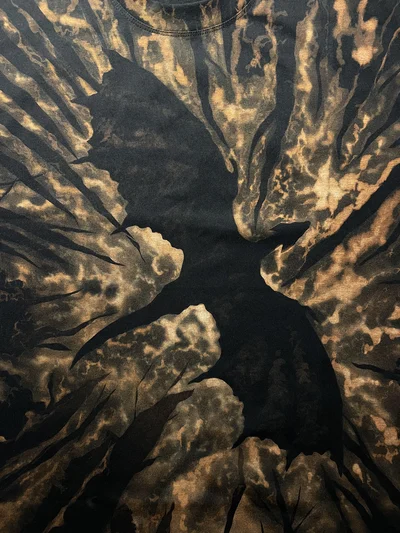 Nahaufnahme der Drachensilhouette und kupferfarbenen Bleach-Art-Details auf einem schwarzen T-Shirt