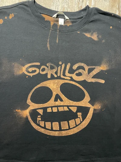 Nahaufnahme des gebleichten Gorillaz Totenkopf Logos und Schriftzugs auf der Vorderseite des schwarzen T Shirts