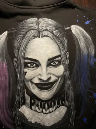 Angled view of a Harley Quinn–inspired hand-painted artwork on the back of a fleece hoodie