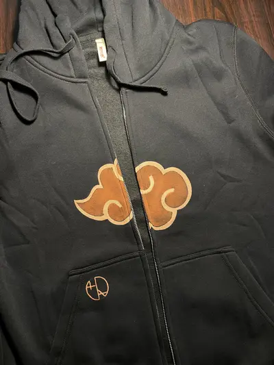 Vorderansicht eines geöffneten Hoodies mit dem durch den Reißverschluss geteilten Emblem der Roten Wolken