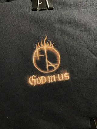 Front view of black hoodie with logo  Helen Oben Art and “God in us” text on the left chest