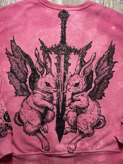 Nähere Ansicht des schwarzen Cybersigilism-Rückenmotivs mit zwei geflügelten Hasen und einem Schwert auf einem rosa Sweatshirt