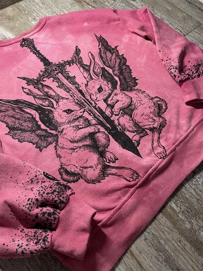 Side view of a pink cybersigilism sweatshirt showing the winged rabbit back design and black paint drips on the sleeve