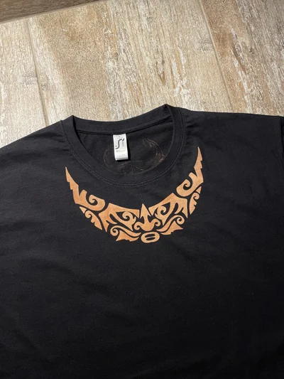 Nahaufnahme des polynesischen Gesichtsmotivs auf der Vorderseite des T-Shirts