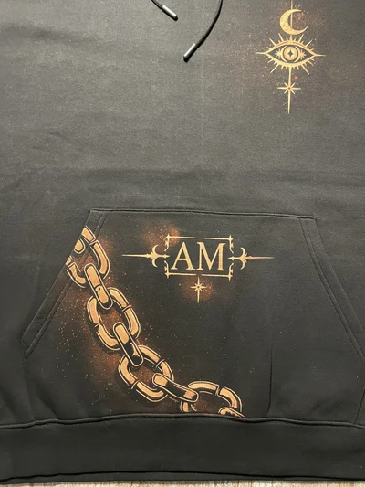 Nahaufnahme des Vorderseitendesigns mit himmlischem Auge, Mondsichel, Initialen und einer Kette über der Bauchtasche