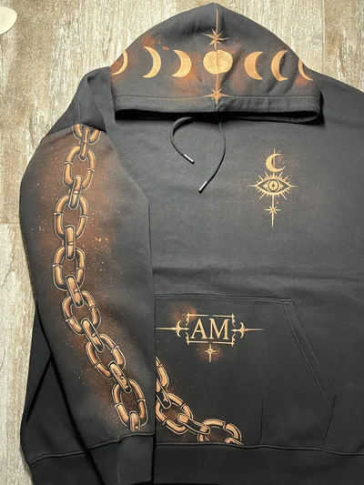 Nahaufnahme der Motive auf Kapuze, Brust und Tasche mit sichtbarem Kettendesign auf dem rechten Ärmel
