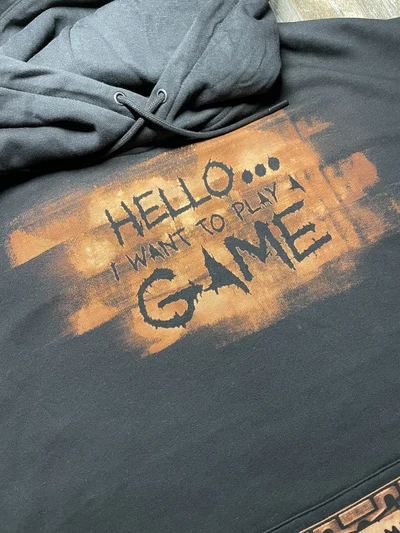 Close up of the hand drawn bleach art cassette with Play Me lettering on the front of a black hoodie