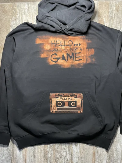 Full front view of a black horror hoodie with a bleach art cassette and the words Play Me and Hello I Want to Play a Game