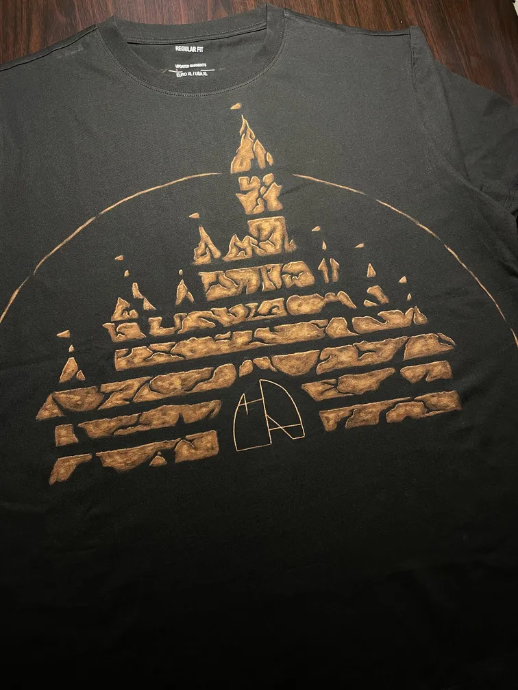 Front view of a t-shirt with a ruined fairy-tale castle illustration and the Helen Oben Art logo