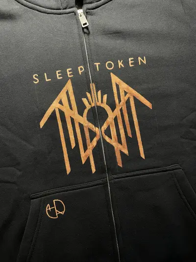 Detail of the Sleep Token logo and text divided into two halves by the central zipper on the hoodie