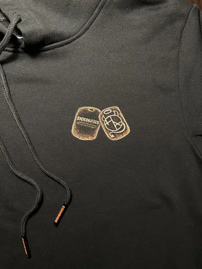 Detail of hand-painted dog tag artwork on the front of a black cotton hoodie