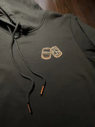 Front view of a hoodie with two military dog tags, one with soldier number and one with Helen Oben Art logo