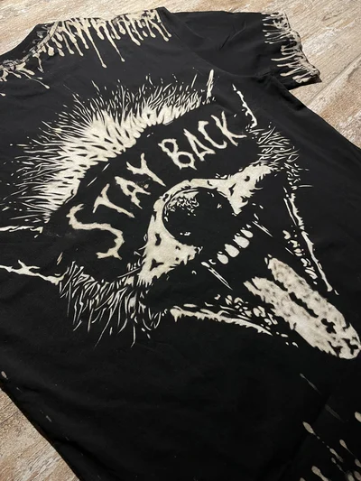 Close-up of handmade raccoon bleach painted design with Stay Back lettering on black grunge tee