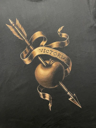 Nahaufnahme des Frontmotivs mit Pfeil, Apfel und Victoria Band auf schwarzem Baumwollshirt